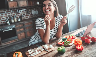 A brunette haired woman in her kitchen cooking vegetables