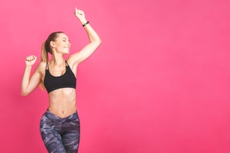 a fit middle aged women jumping in front of a pink background