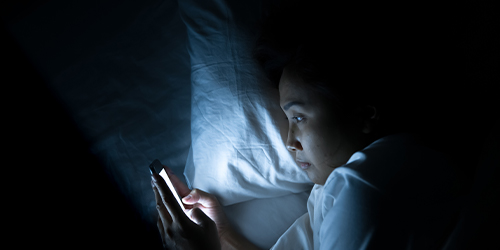 Asian woman laying in bed looking at cellphone
