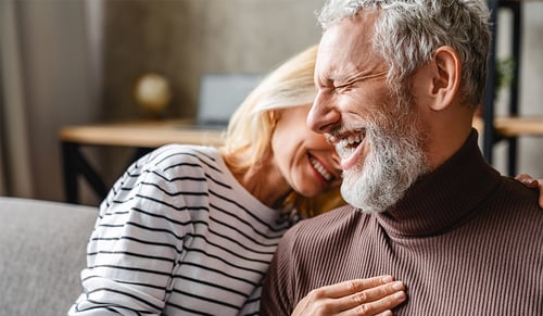 Happy laughing middle aged couple bonding while relaxing sitting on sofa