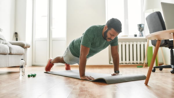 Male fitness instructor showing push up exercises while streaming, broadcasting video lesson on training at home using laptop.