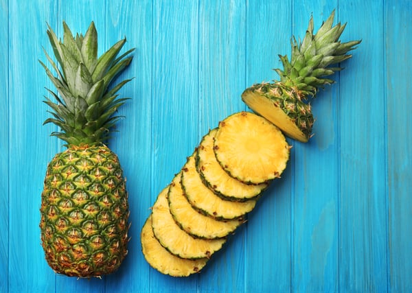 Slices of ripe pineapple and whole fruit on wooden background