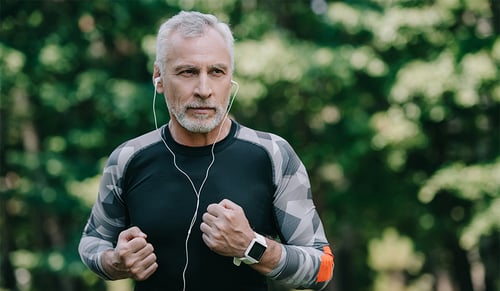 handsome mature sportsman listening music in earphones while running in park