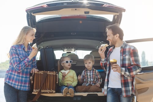 Family eating snacks behind their car